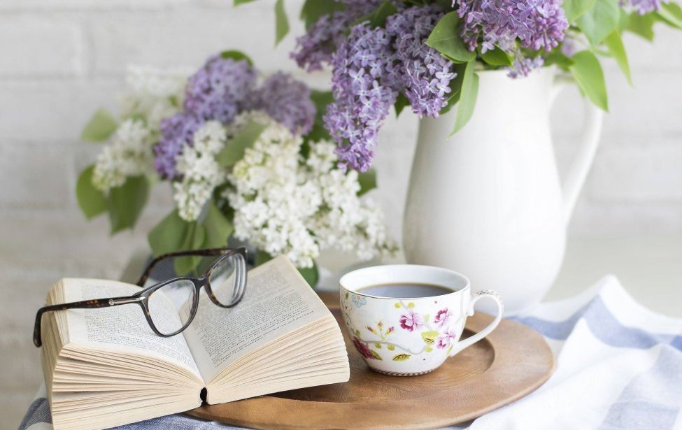Aufgeschlagendes Buch, eine Lesebrilole und eine Tasse Kaffee