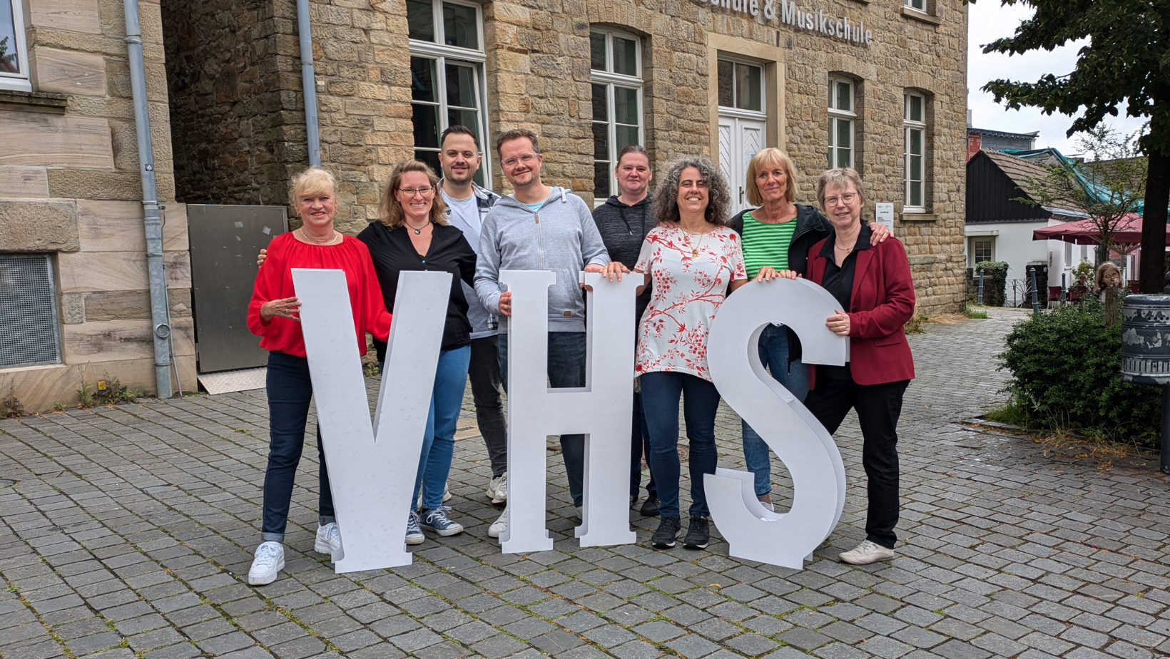 Foto des Teams der vhs mit Pappaufstellern vor dem Gebäude in Blankenstein.