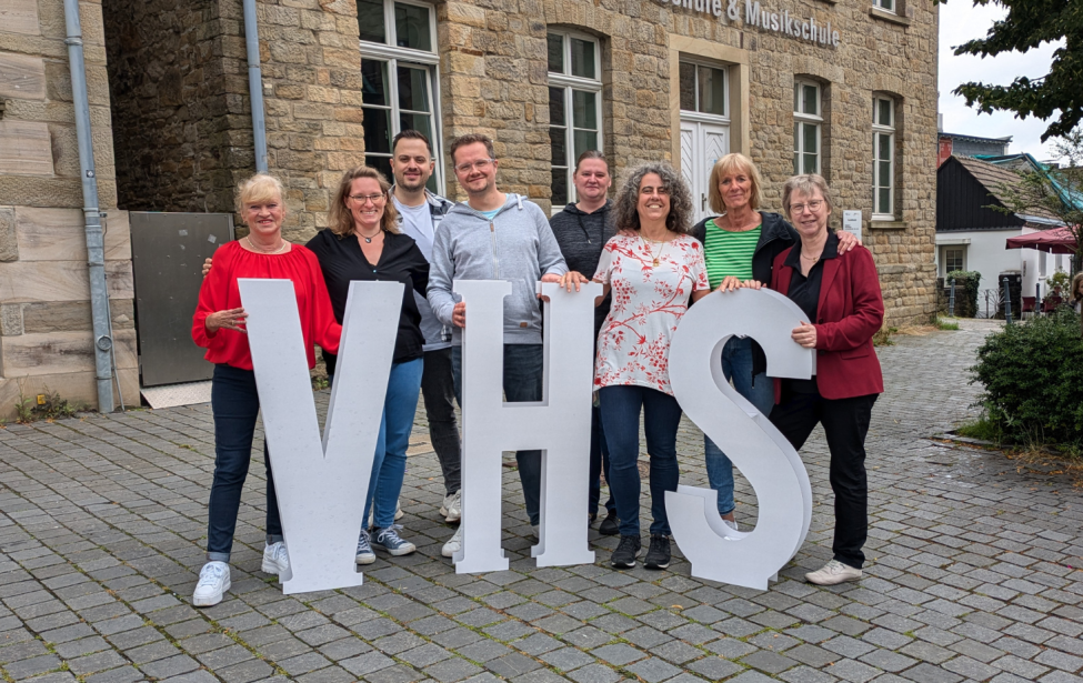 Foto des Teams der vhs mit Pappaufstellern vor dem Gebäude in Blankenstein.