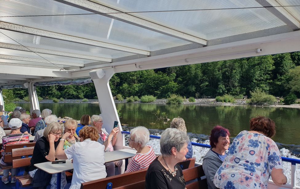 Teilnehmende Senioren sitzen in einem Schiff. Im Hintergrund ist das Ruhrufer zu sehen.