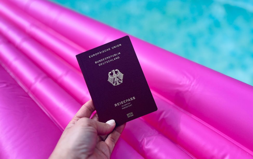 Hand hält Reisepass, im Hintergrund Luftmatratze im Pool