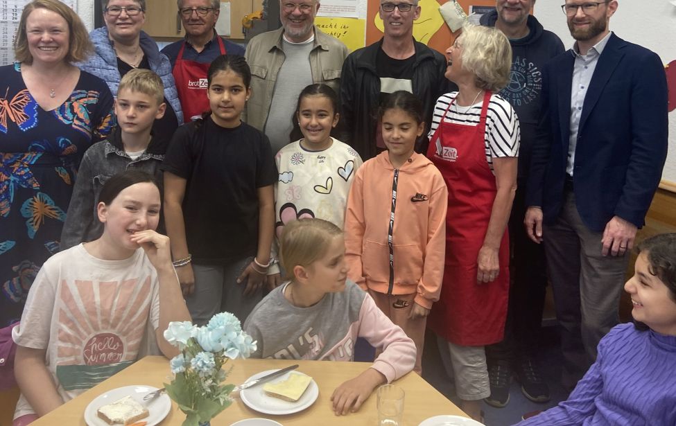 Kinder am Tisch beim Frühstück im Hintergrund eine Menschengruppe