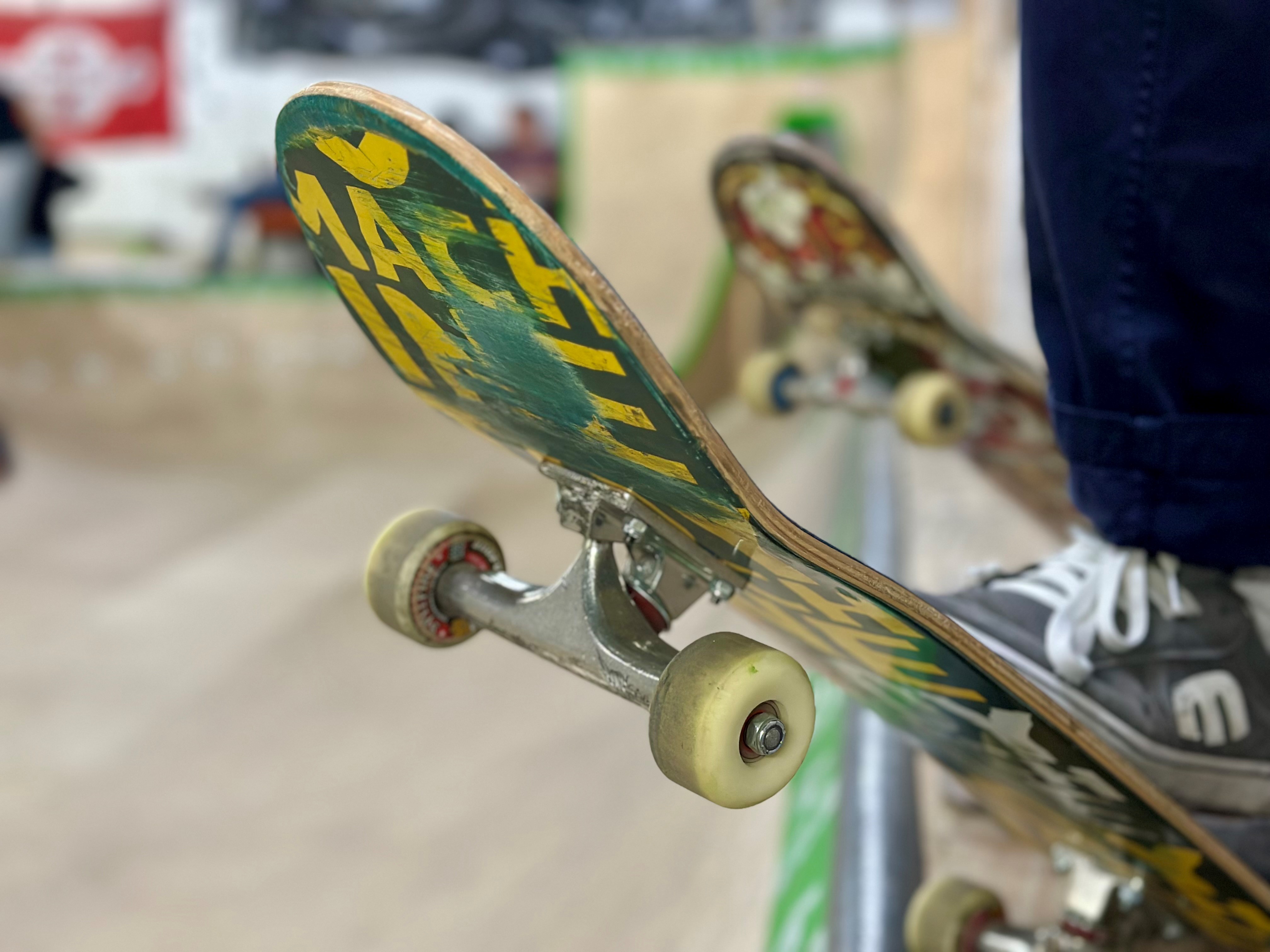Nahaufnahme eines Skateboards. Im Hintergrund ist unscharf eine Rampe zu sehen.