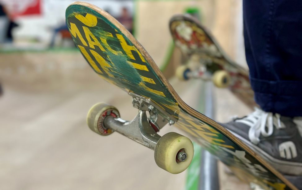 Nahaufnahme eines Skateboards. Im Hintergrund ist unscharf eine Rampe zu sehen.