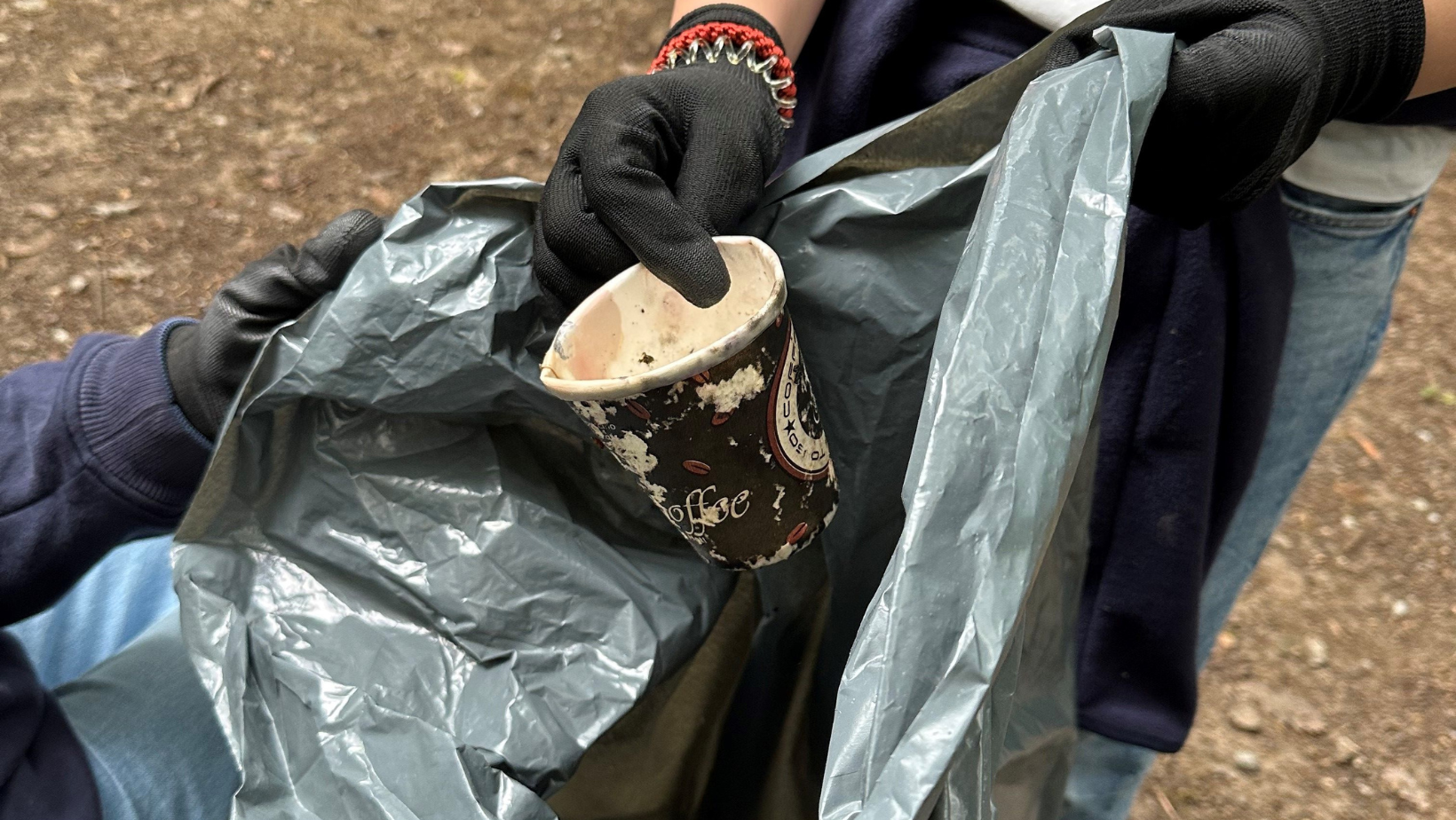 Fotografie eines alten Kaffebechers, welcher in einen Müllsack getan wird