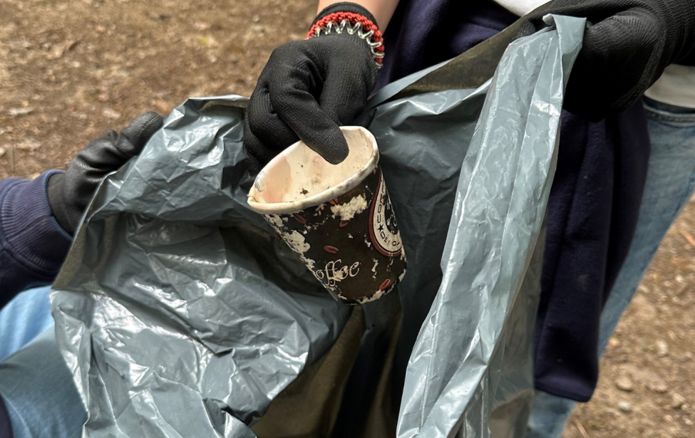 Fotografie eines alten Kaffebechers, welcher in einen Müllsack getan wird