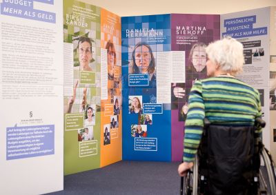 Fotografie einer Person mit Rollstuhl, die sich die Aufsteller ansieht